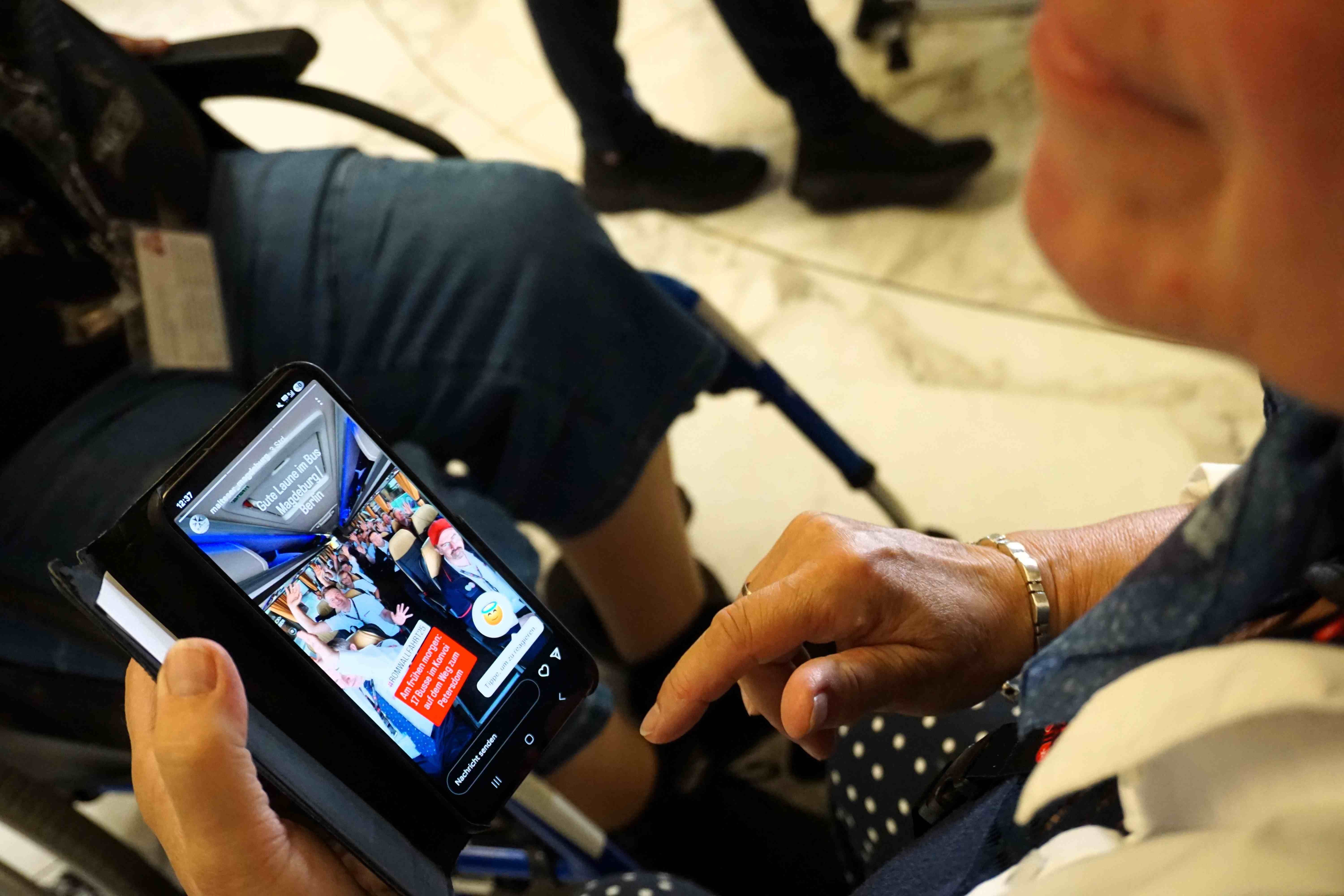 Person hält Smartphone mit sichtbarem Bildschirm, auf dem eine bunte Benutzeroberfläche zu sehen ist.