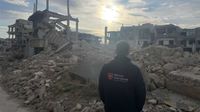 Ein Mann mit einer Jacke von „Malteser International“ steht mit dem Rücken zur Kamera vor einer Gebäuderuine in Syrien.