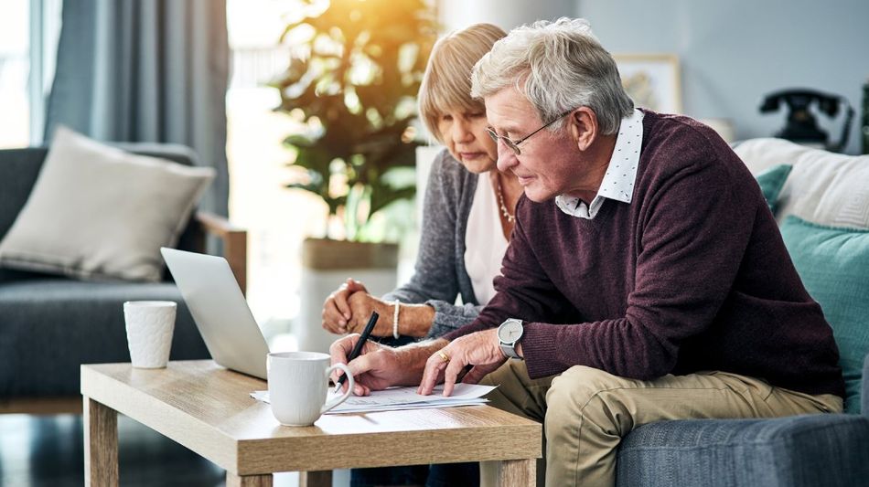 Ein älteres Paar mit Laptop und Papieren im Wohnzimmer