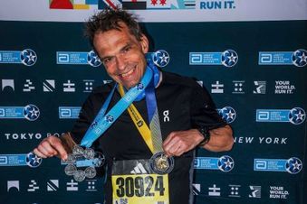 Mann in Sportkleidung posiert stolz mit zwei Medaillen vor einer Wand des Abbott World Marathon Majors.