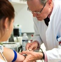 Zu sehen ist eine Patientin von der Seite mit ausgestrecktem Arm, der von einem Arzt Blut abgenommen wird. 