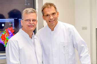 Zwei Ärzte in weißen Kitteln stehen nebeneinander in einem medizinischen Raum.