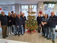 Die ehrenamtlichen Helfer stehen als Team zusammen vor dem geschmückten Weihnachtsbaum. 