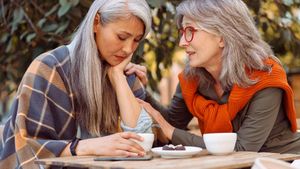 Zwei ältere Frauen unterhalten sich an einem kleinen Tisch im Außenbereich eines Cafés.