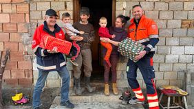 Zwei Malteser stehen mit einer Familie mit zwei Kindern vor einem Haus im Rohbau.