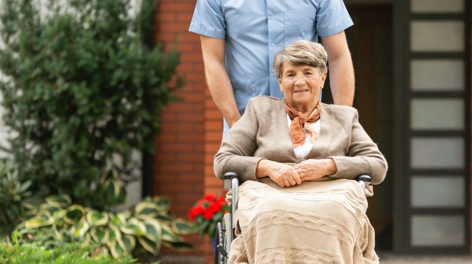 Eine ältere Frau im Rollstuhl wird von einem Mann geschoben.