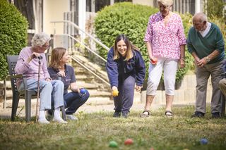 Damen in Malteser Kleidung spielen auf einer Wiese mit Senioren ein Ballspiel