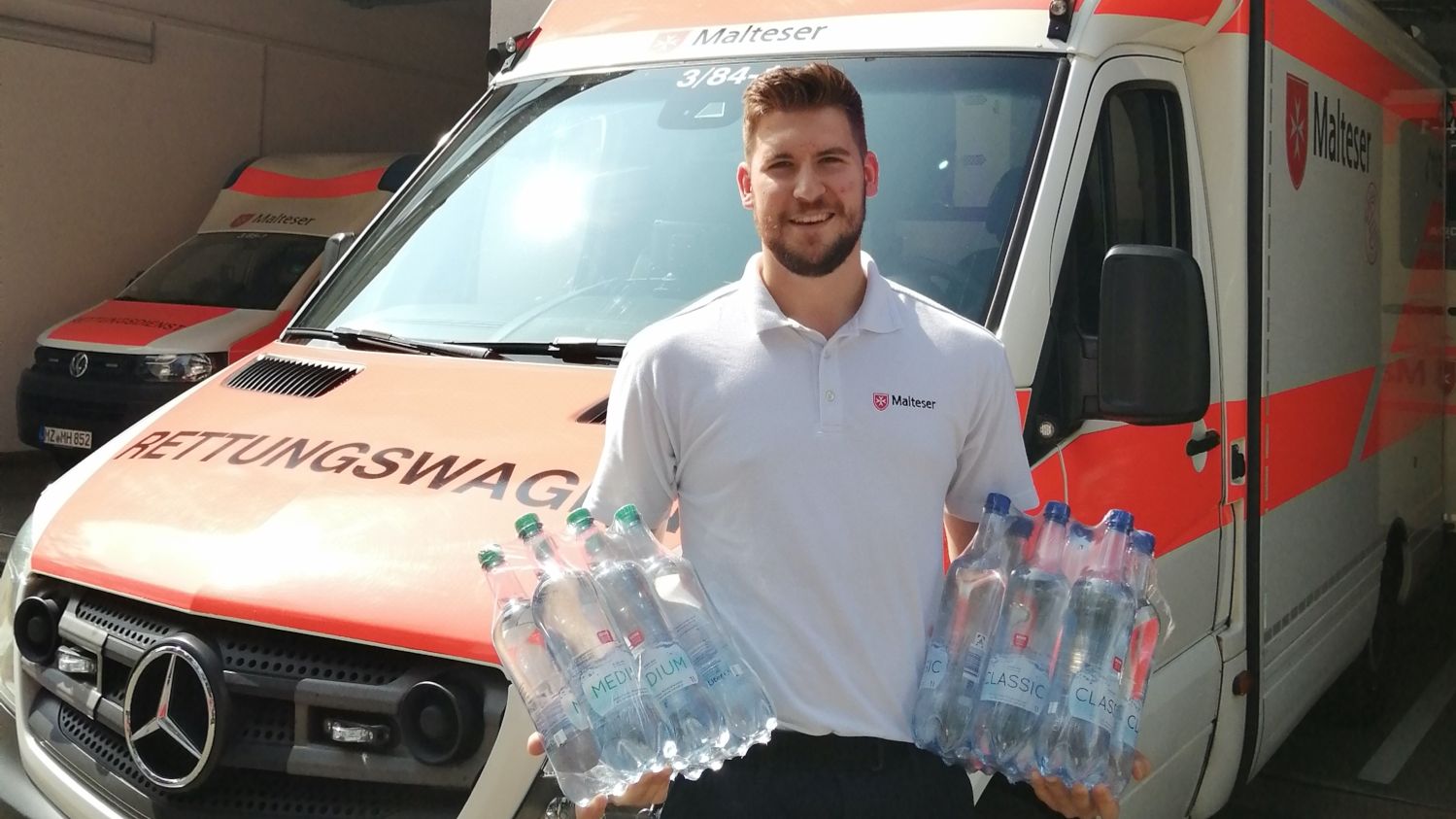 Junger Mann mit Wasserflaschen vor Rettungswagen