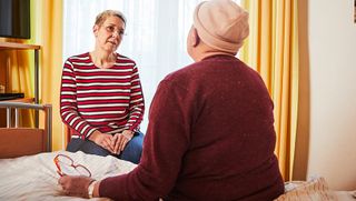 Eine Mitarbeiterin in einem Hospiz spricht mit einer Bewohnerin in deren Zimmer. 