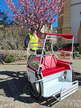Mann sitzt auf Elektro-Rikscha-Fahrrad vor blühendem Baum