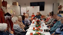 Viele, meist ältere Menschen sitzen um einen adventlich geschmückten Tisch, daneben steht ein Nikolaus.