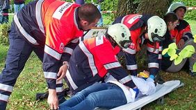 Mehrere Malteser Helfer in Einsatzkleidung versorgen bei einer Übung eine Person, die auf einer Trage liegt.