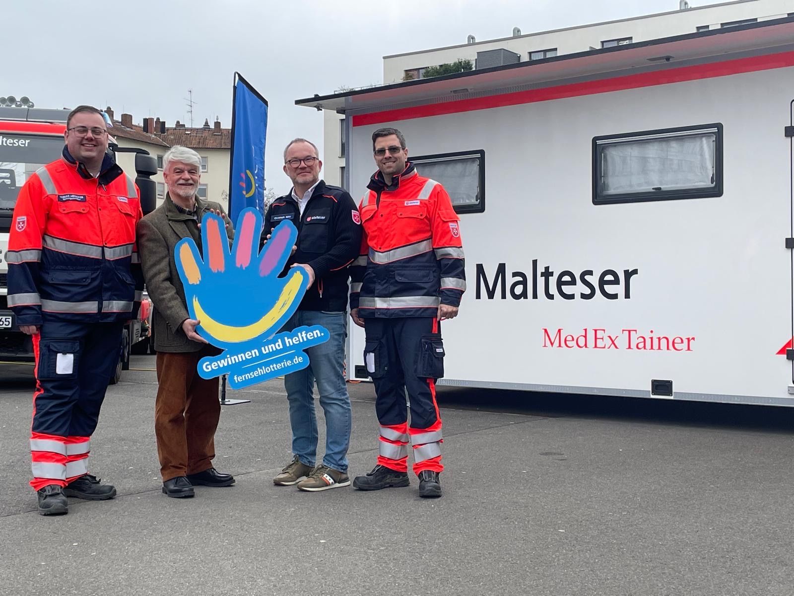 Auf dem Foto sieht man 4 Personen vor dem aufgebauten MedExTainer. Zwei Personen tragen dabei Einsatzkleidung der Malteser