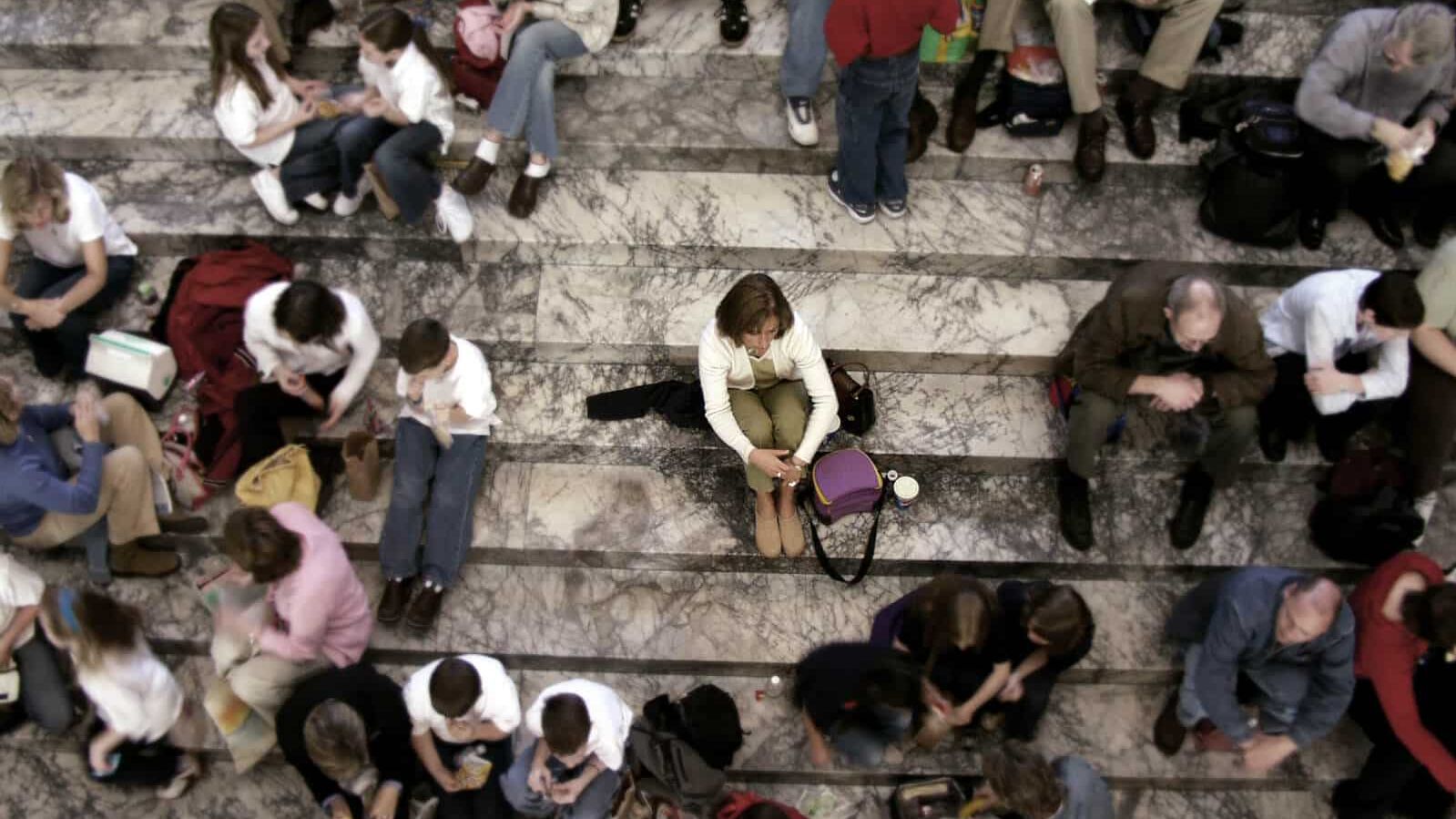 Gruppe von Menschen sitzen auf einer Treppe, eine Person sitzt isoliert