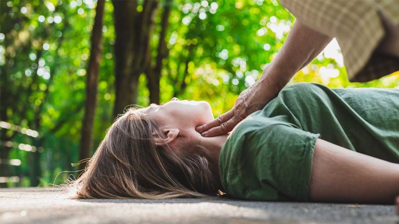 Eine ältere Frau überprüft den Puls eines jüngeren, bewusstlosen Mädchens.