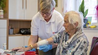 Mitarbeiterin im Pflegedienst legt einer älteren Dame zu Hause einen Verband an