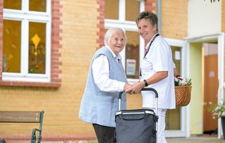 Zwei Frauen stehen vor einer Einrichtung mit einem Einkaufswagen und lächeln in die Kamera