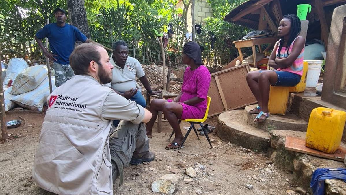 Fünf Menschen sitzen zwischen Trümmern und Müll in Haiti.