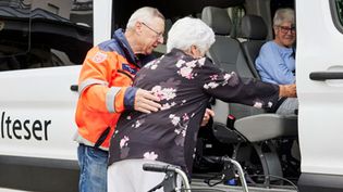 Ein Helfer der Malteser hilft einer Frau beim Einsteigen in ein Fahrzeug