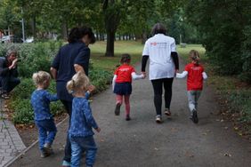 Zwei Mitarbeiterinnen der Malteser laufen mit Kindern an den Händen im Park.