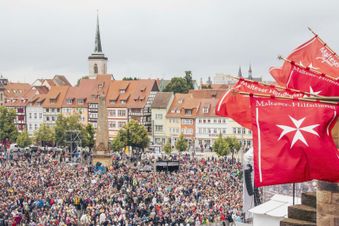 Menschen schwenken Fahnen der Malteser