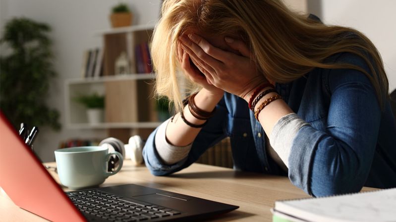 Frau im Homeoffice lehnt das Gesicht verzweifelt in die Hände 