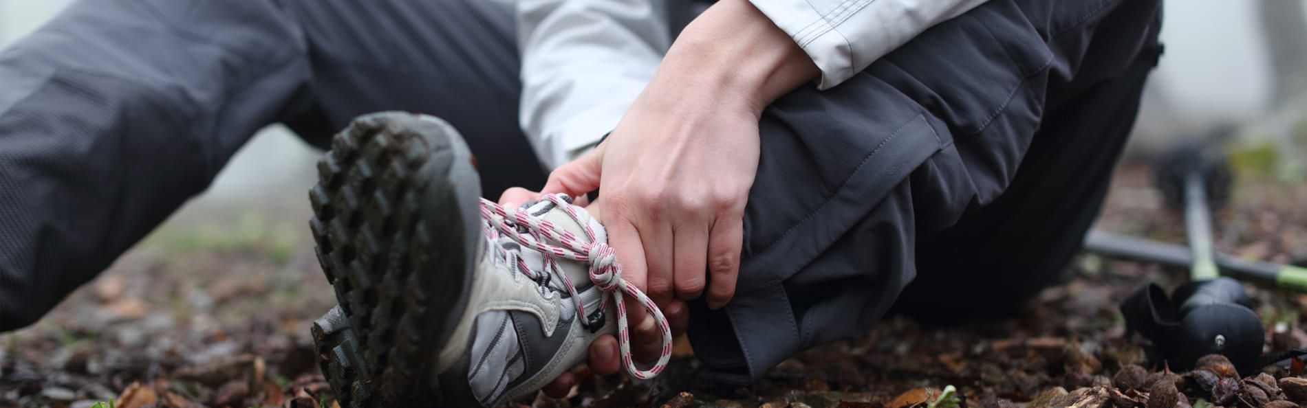 Ein Mann in Outdoor-Kleidung sitzt auf einem Waldboden und hält sich den Fußknöchel.