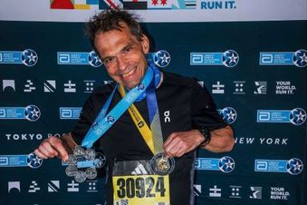 Mann in Sportkleidung posiert stolz mit zwei Medaillen vor einer Wand des Abbott World Marathon Majors.