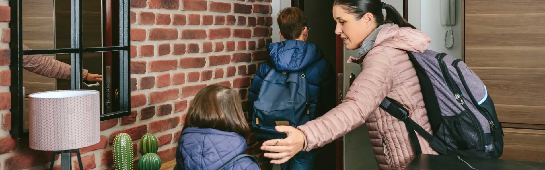 Eine Frau und zwei Kinder mit Rucksäcken verlassen eine Wohnung.
