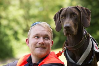 Mann in Malteserkleidung schaut lächelnd zu einem großen braunen Hund mit Schlappohren auf