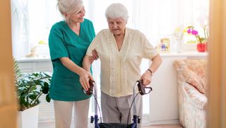Eine Pflegerin hilft einer älteren Dame mit Rollator beim gehen