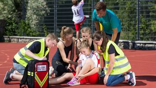 Malteser Schulsanitäter versorgen ein Mädchen, das sich beim Sport verletzt hat.