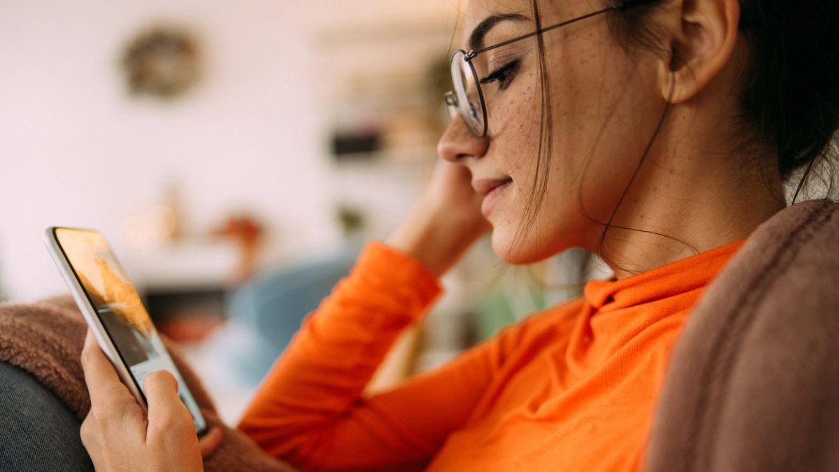 Junge Frau mit Brille schaut auf ein Smartphone.