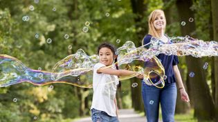 Junge macht große Seifenblasen und wird von Malteser Helferin begleitet.