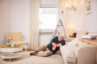 Eine Dame liegt an ein Sofa gelehnt und bekommt Hilfe von einer Helferin des Malteser Hausnotruf 