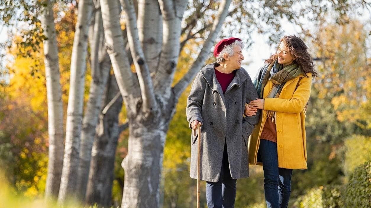 Eine junge Frau und eine ältere Frau mit Gehstock bei einem Herbstspaziergang.