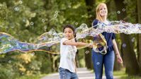 Eine junge, lächelnde Frau und ein Mädchen machen Seifenblasen.
