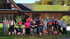 Viele Menschen und einige Hunde stehen vor einem Haus.