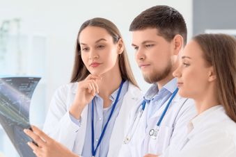 Drei Ärzte betrachten gemeinsam eine Röntgenaufnahme und diskutieren die Diagnose.