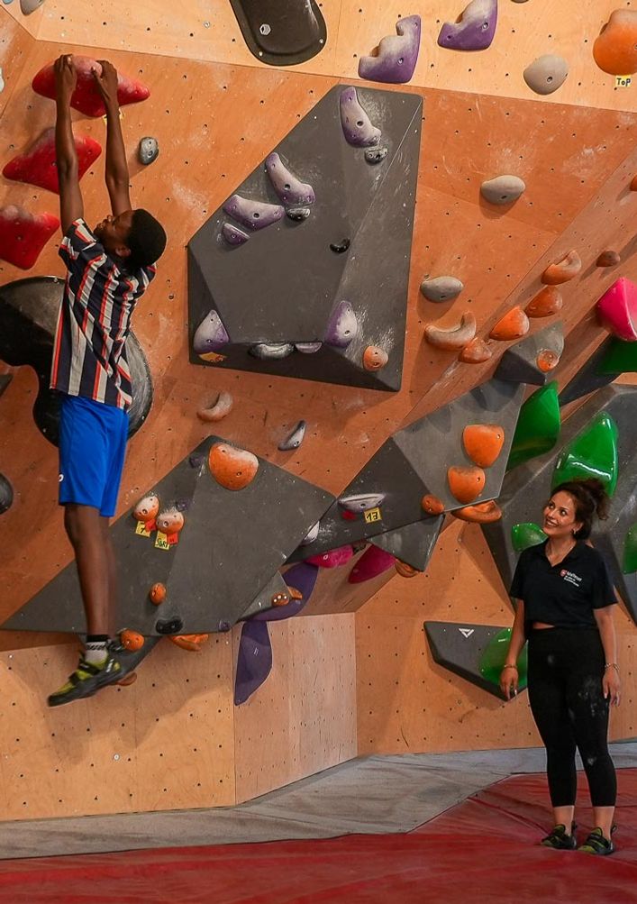 Gruppe des Malteser Integrationsprojekts schaut zu, wie ein Teilnehmer eine Boulderwand erklimmt.