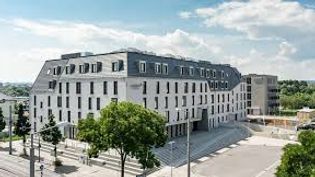 Modernes Hotelgebäude mit heller Fassade und Vorplatz in urbaner Umgebung.