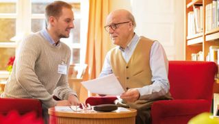 Zwei Männer sitzen nebeneinander am Tisch und unterhalten sich über Dokumente