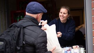 Malteser Helferin reicht Hilfsbedürftigem eine Lebensmitteltüte.