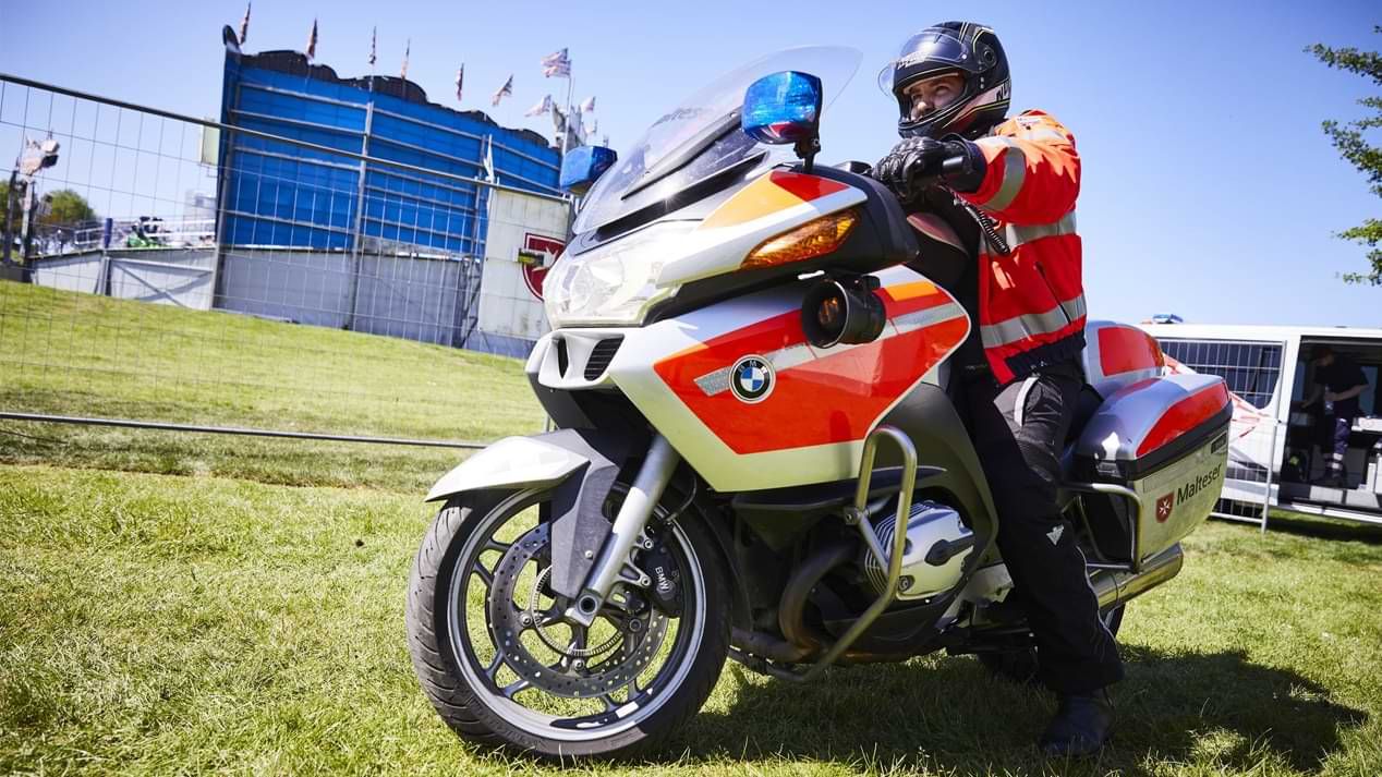 Ein Mann in orangefarbener Einsatzkleidung auf einem Motorrad