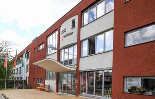 Ein rotes und graues Gebäude mit dem Schild "Malteser" und einem überdachten Eingang.