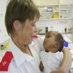 A care worker holds an infant in her arms.