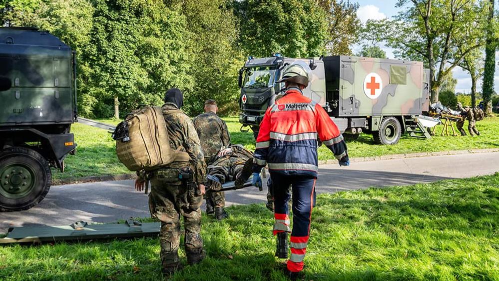 Zwei Soldaten der Bundeswehr und ein Helfer des Malteser Rettungsdienstes transportieren einen Soldaten auf einer Trage.