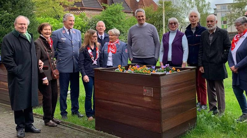 Elf Menschen, zum Teil in Kleidung des Malteser Hilfsdienstes, vor einem Hochbeet mit Blumen.