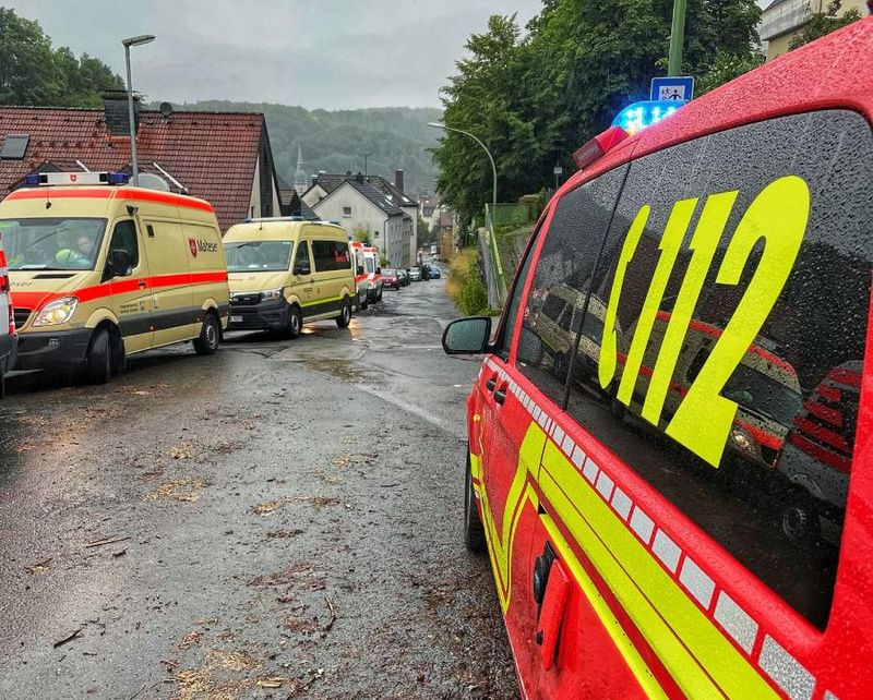 Einsatzfahrzeuge parken beidseitig an einer nassen Straße.