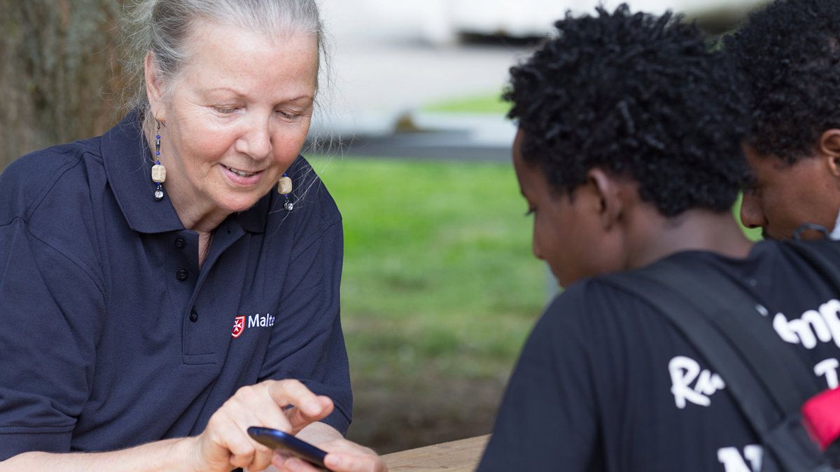 Ältere Frau zeigt jungen Flüchtlingen etwas auf dem Smartphone.